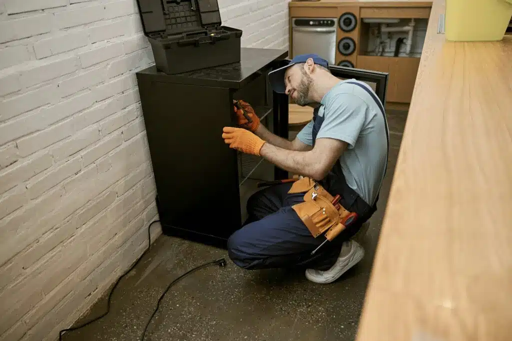 Bearded young man repairing fridge in kitchen