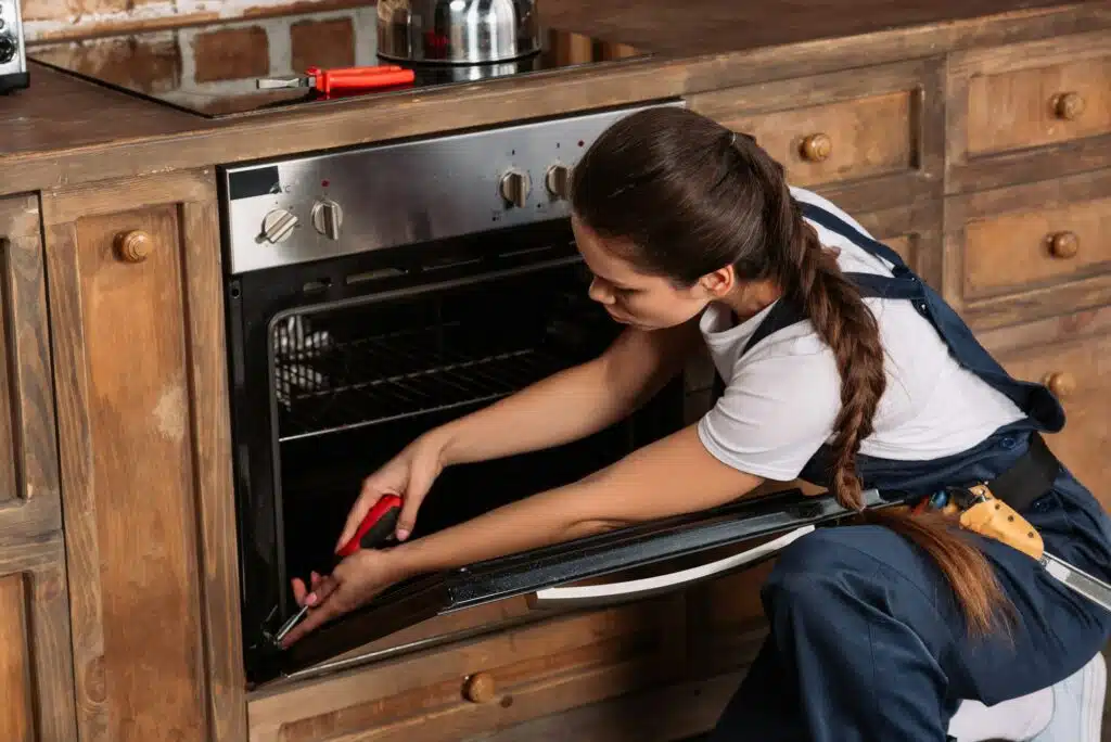 young repairwoman repairing oven with screwdriver